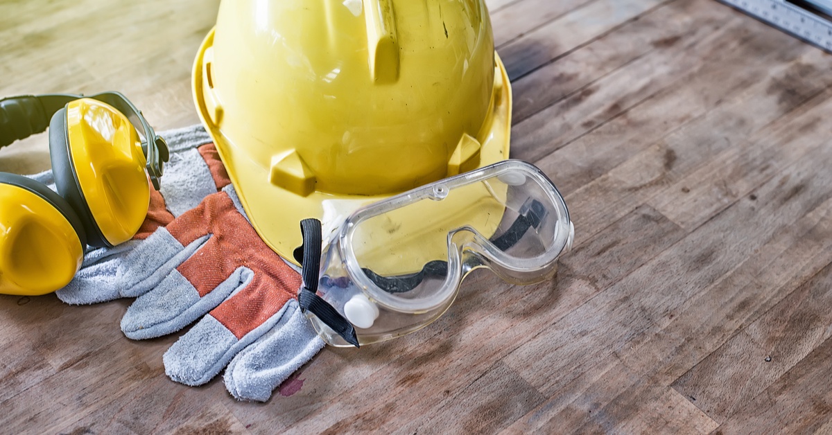 Protective equipment, including a hard hat, safety glasses, gloves, and earmuffs sit on a wooden table.