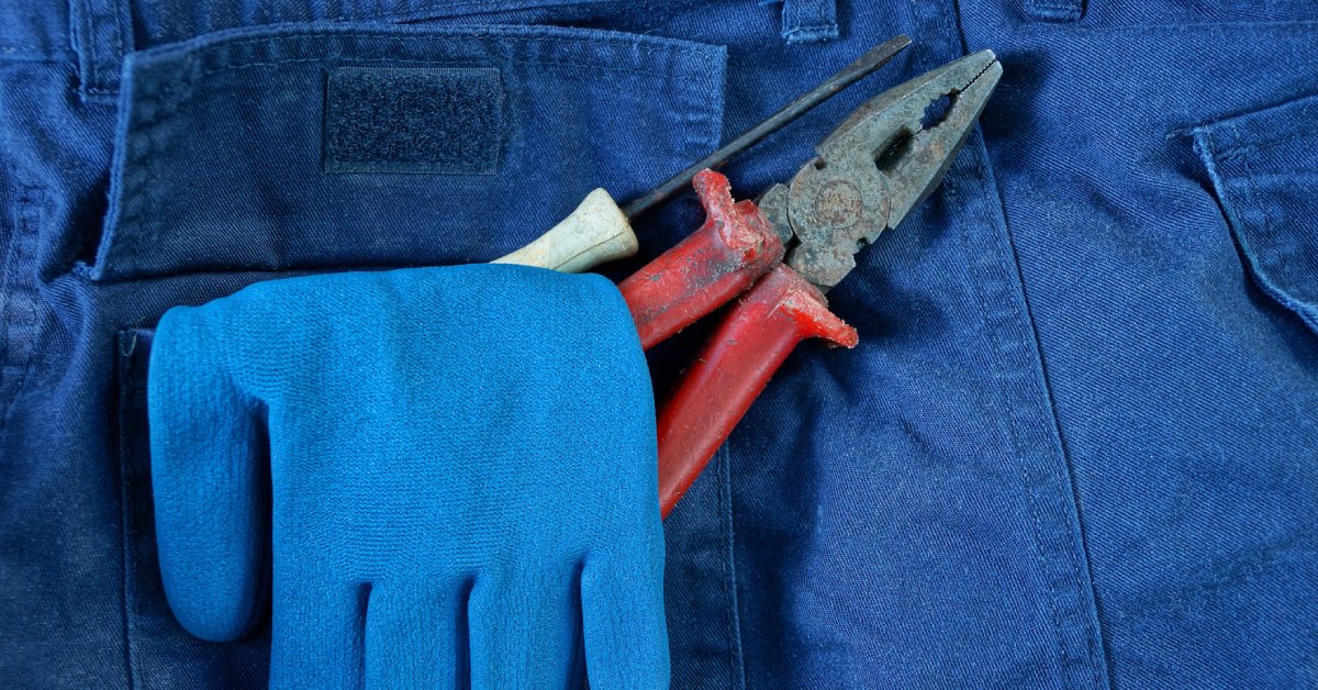 The pocket of a pair of blue pants has a pair of pliers, a blue glove, and a screwdriver sticking out of it.