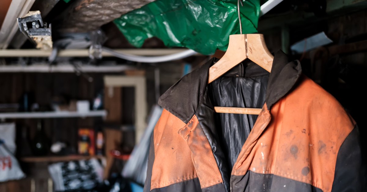 An orange and black jacket hanging on a wooden hanger is dirty, with black stains visible on the orange parts.