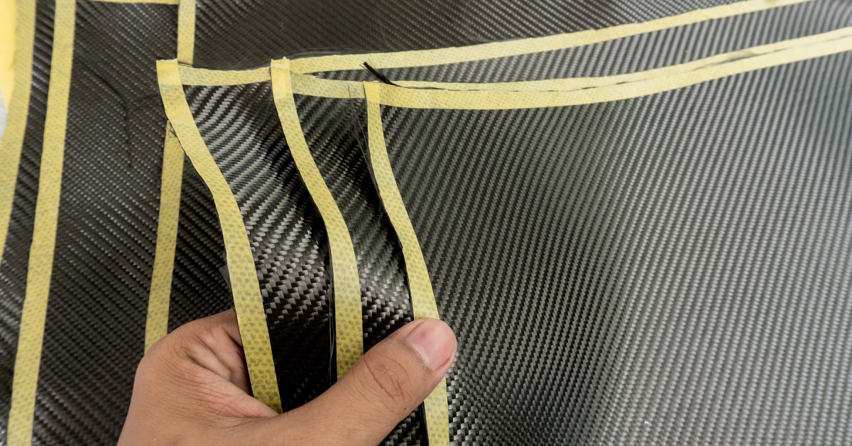 A close-up of a hand holding multiple sheets of shiny black fabric with yellow trim stacked together.