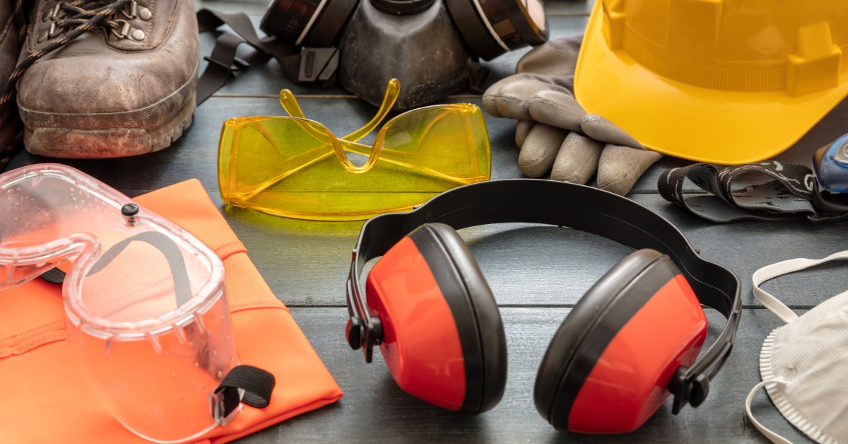 Different protective accessories for the workplace, including earmuffs and eye goggles on a wooden table.