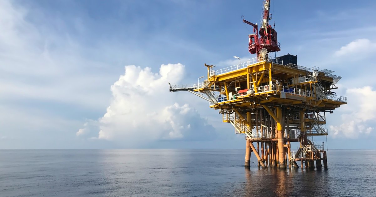A yellow offshore oil platform stands out in the calm ocean water under a blue, cloudy sky on a clear day.