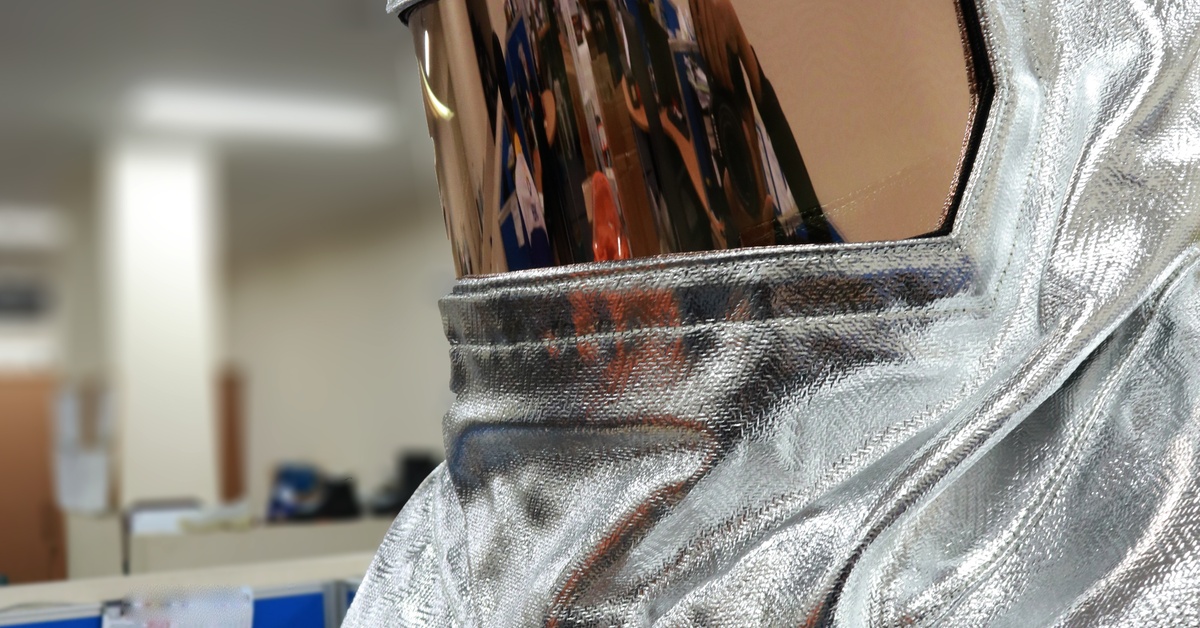 A person is wearing a silver, fireproof suit. The suit has a helmet with an opaque visor. They are inside a building.