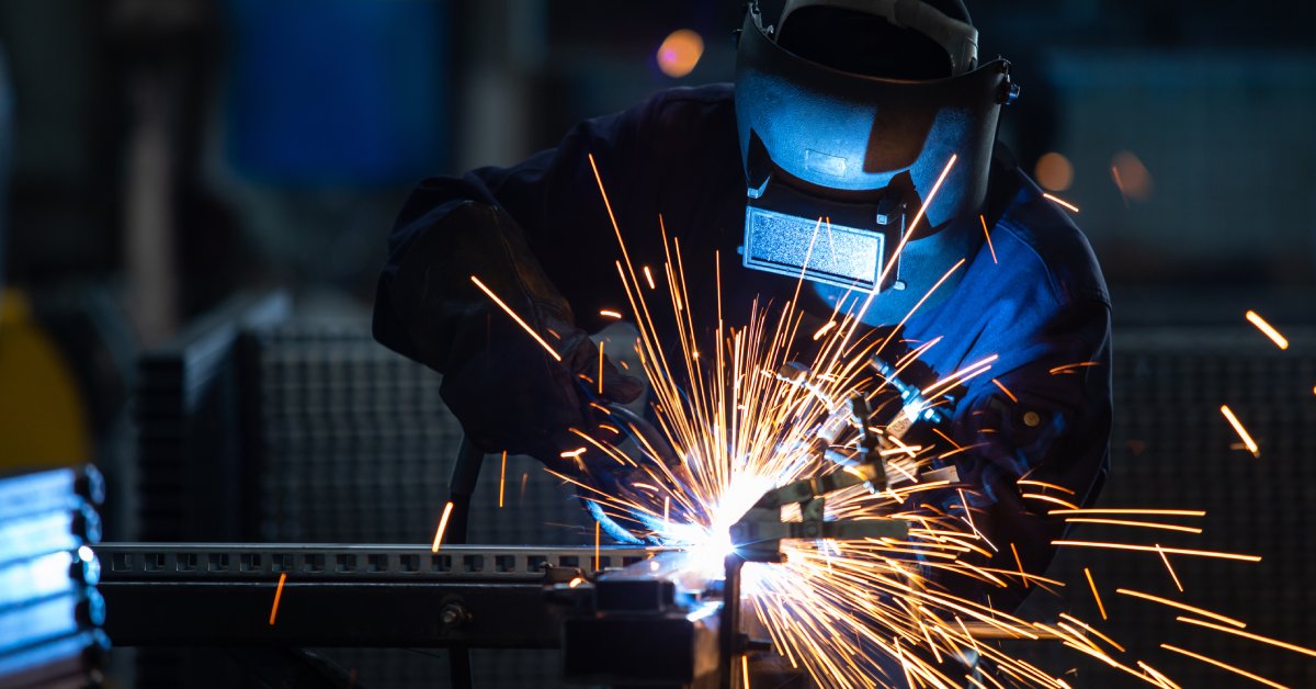 A person is using a welding machine on pieces of metal. They are wearing a protective mask on their head.