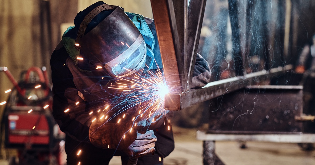A person using a welding machine. They are wearing a protective mask on their face and are bending over to weld an object.