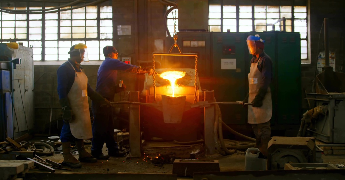 Three people are standing next to a fire, they are all wearing aprons, two of them are wearing protective face shields.