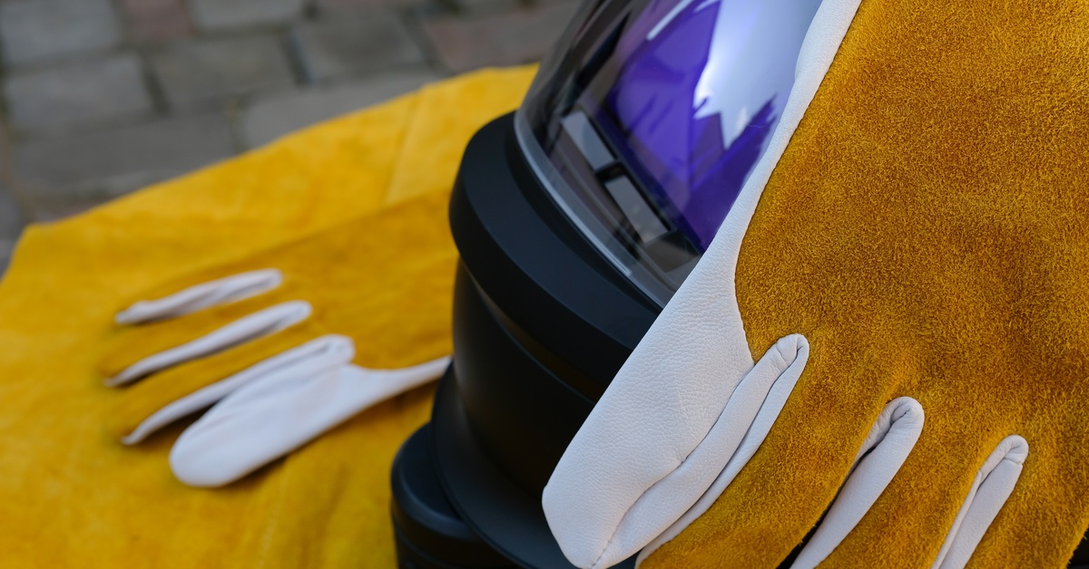 A yellow glove is placed over a helmet. The helmet has a large, reflective visor. There is a pile of yellow material under the helmet.