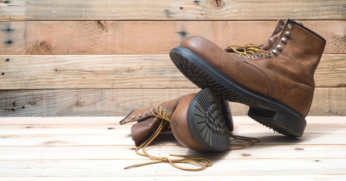 A pair of boots are sitting on a wooden surface. The wall behind the boots is also made out of wood.