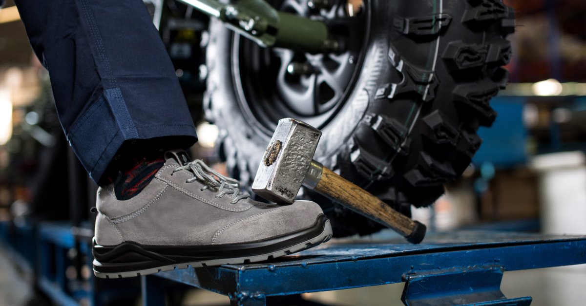 A person has their foot up on a ledge. There is a hammer laying against their foot. There is a tire in the background.