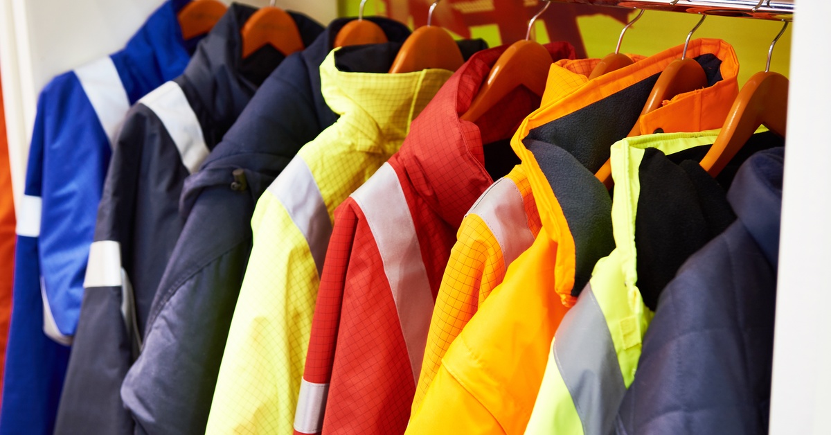 Different fire-resistant jackets in various colors hang on a rack together for industrial workers to use.
